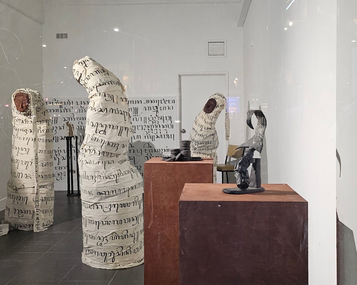 Addin Sugarda, ‘Anugerah: (Bestowed)’ at HAIR ARI. The exhibition shot through a glass window, with large figures wrapped in Muslim cloth, decorated with poetry.