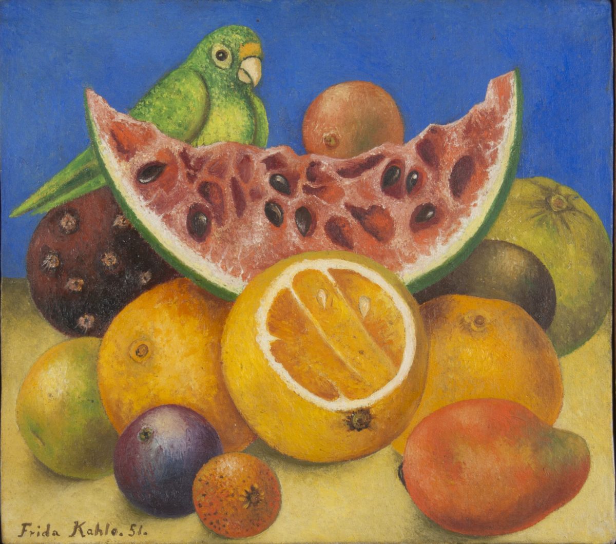 A painted still life of a large slice of watermelon surrounded by oranges and other spherical tropical fruits, with a green parrot behind on a yellow table top and blue background. Frida Kahlo