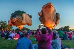 Two surreal animal shaped hot air balloons with people in park watching. Skywhales