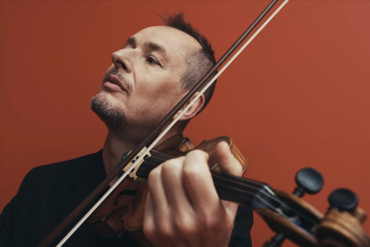 Up close photo of man playing violin against red background. ACO Richard Tognetti