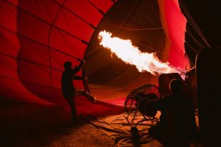 On The Move is ArtsHub's weekly round-up of Australian arts sector appointments from around the country. The photo depicts a hot air balloon being prepared for flight. Taken before dawn, the focus of the photo is the gas jet of flame generatng the heat required to inflate and fly the balloon.