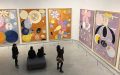 An exhibition of large paintings depicting circular shapes with vibrant colours, while four viewers look on.