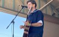A young man in a blue shirt with an acoustic guitar plays on a small outdoor stage with his eyes closed. Flynn Gurry. Port Fairy Folk Festival.