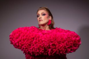 Geraldine Quinn's 'Bastard Joy' at Melbourne International Comedy Festival 2025. A publicity image for the show: Quinn, a fair-skinned woman with swept-back, shoulder-length auburn hair, stares dramatically at the camera. She wears an ornate ruffled dress in hot pink, and large, half-moon pink earings to match.