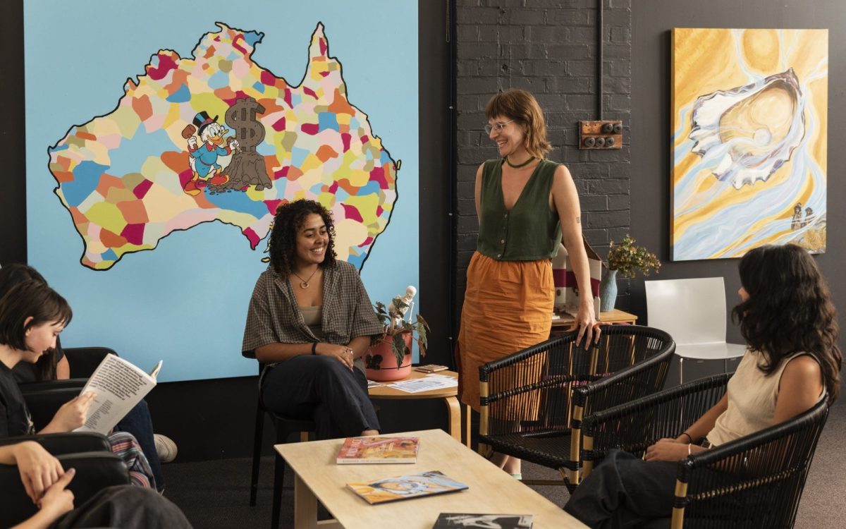 Students and a single staff gathering around a table with a map of Australia in the background. The atmosphere is welcoming and friendly.