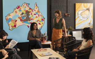 Students and a single staff gathering around a table with a map of Australia in the background. The atmosphere is welcoming and friendly.