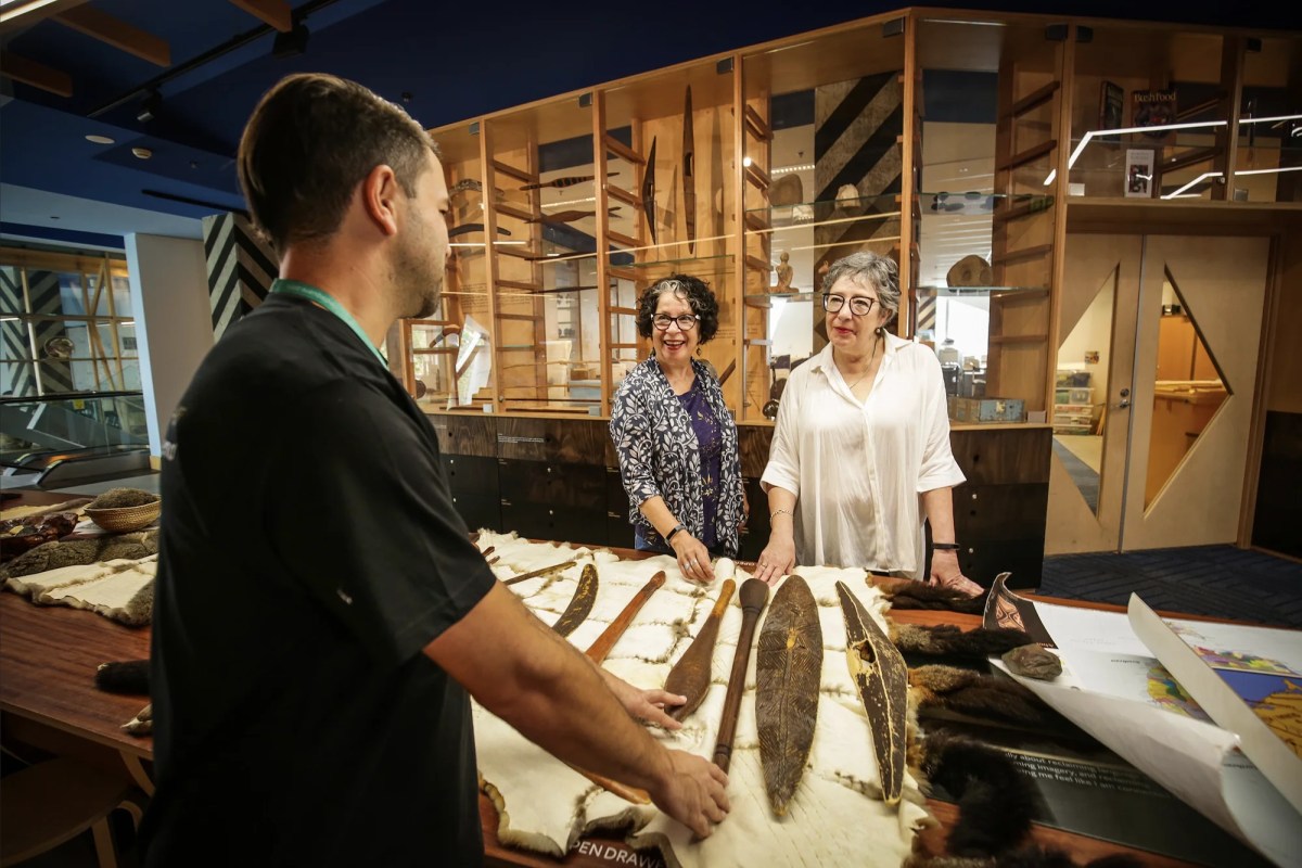 Man talking to two women over table with Aboriginal artefacts. Koori Heritage Trust