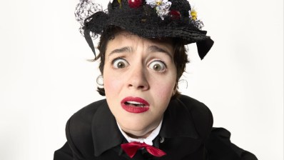 Close up of a young woman wearing black with a red bow tie and an elaborate bonnet.