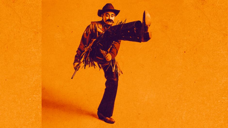 Against a yellow background, a woman dressed as a man dressed in a cowboy costume has one of his legs in the air, mid kick.
