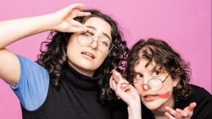 Two young women with curly brown hair and holding their glasses askew.