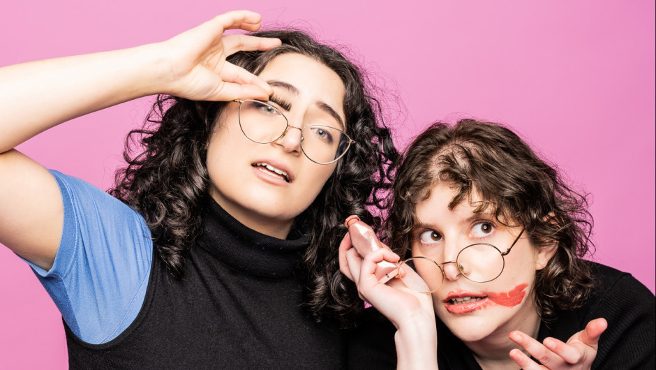Two young women with curly brown hair and holding their glasses askew.