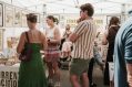 A man in a stripey shirt and some women are looking at art in a light filled tent-like environment.