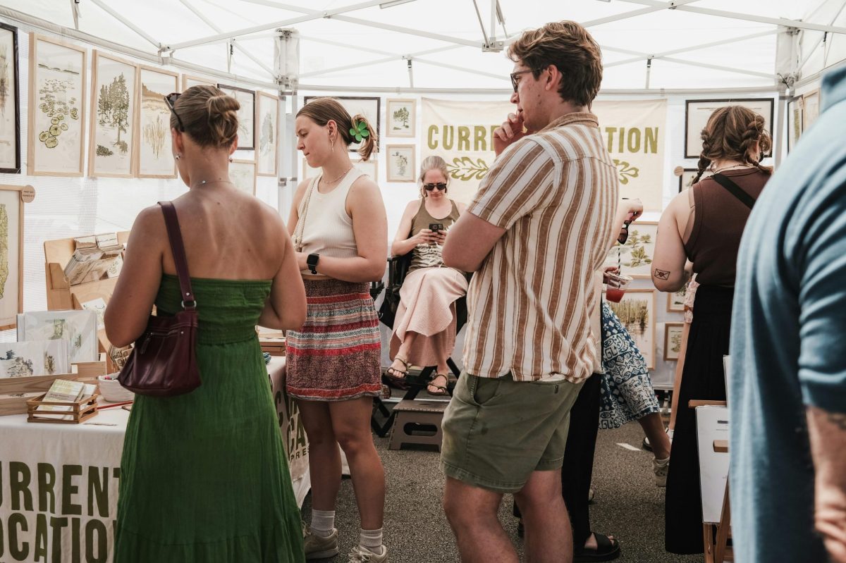 A man in a stripey shirt and some women are looking at art in a light filled tent-like environment.