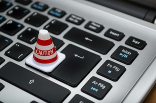 Image of laptop keyboard, with small warning traffic cone. Journalism