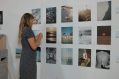 Lady stands in front of exhibition of surf images hung on wall.