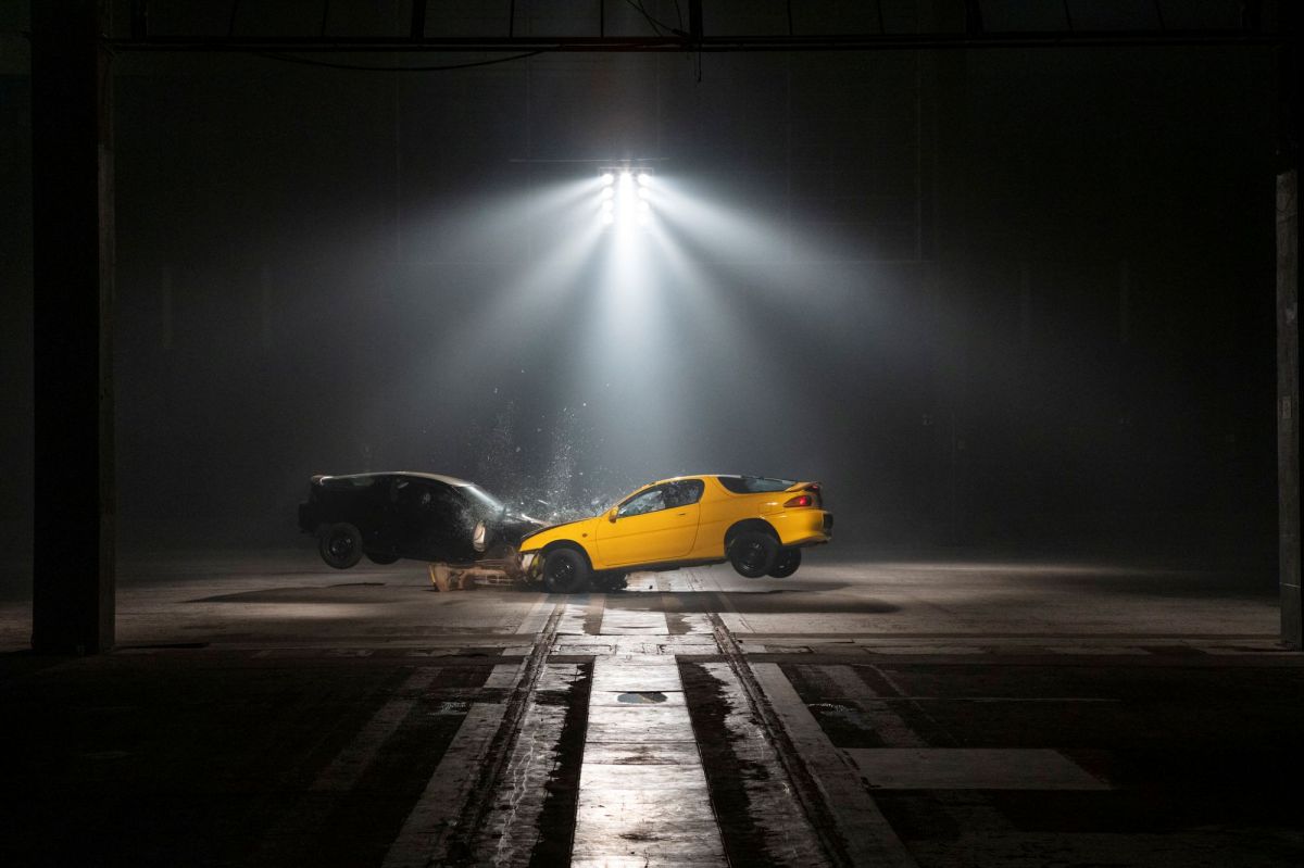'Crash Body' by Paula Garcia, Dark Mofo 2025. Two cars, one yellow, one black, collide head-on under spotlights in a dramatic, moodily-lit photograph.