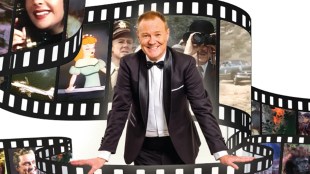 A man in a tuxedo (Stephen Hall) leans forward as film loops around him showing scenes from films featured in his show
