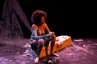 A woman sitting on a bench made of clay. She is also covered in clay.