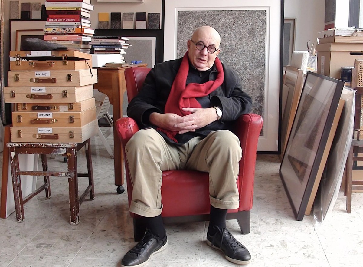 Bald man in black jumper sitting in red chair in artist studio. Allan Mitelman.