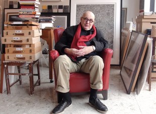 Bald man in black jumper sitting in red chair in artist studio. Allan Mitelman.