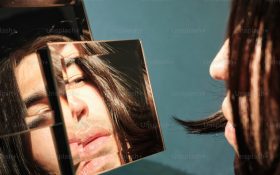 A man with brown hair staring at his reflection in a square of glass.