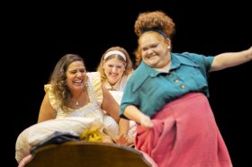 Three women are laughing and sitting together on a bed.