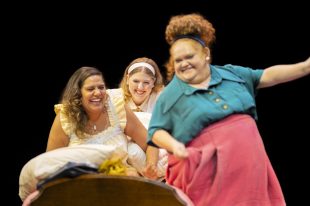 Three women are laughing and sitting together on a bed.