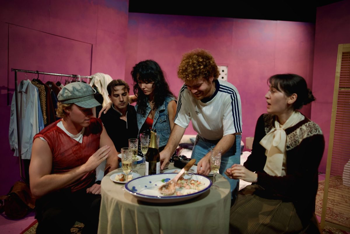 Three young men and a two young women are gathered around a meal on a small table. All of them, aside from the woman on the right, are dressed in casual clothes. She's dressed more primly and conservatively. Dear Elena Sergeevna