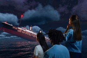 Two young woman and a man are staring at a ship sinking.