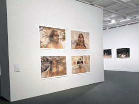 de-centre re-centre: installation view of a photographic exhibition in a gallery space. Four landscape orientation photographs of faces of Aboriginal women are placed on a wall in the foreground of this image.