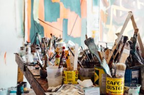 Artist table in studio covered with paintbrushes. Money tips for artists