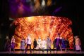 The cast of "Annie" standing against a bright, blazing backdrop.