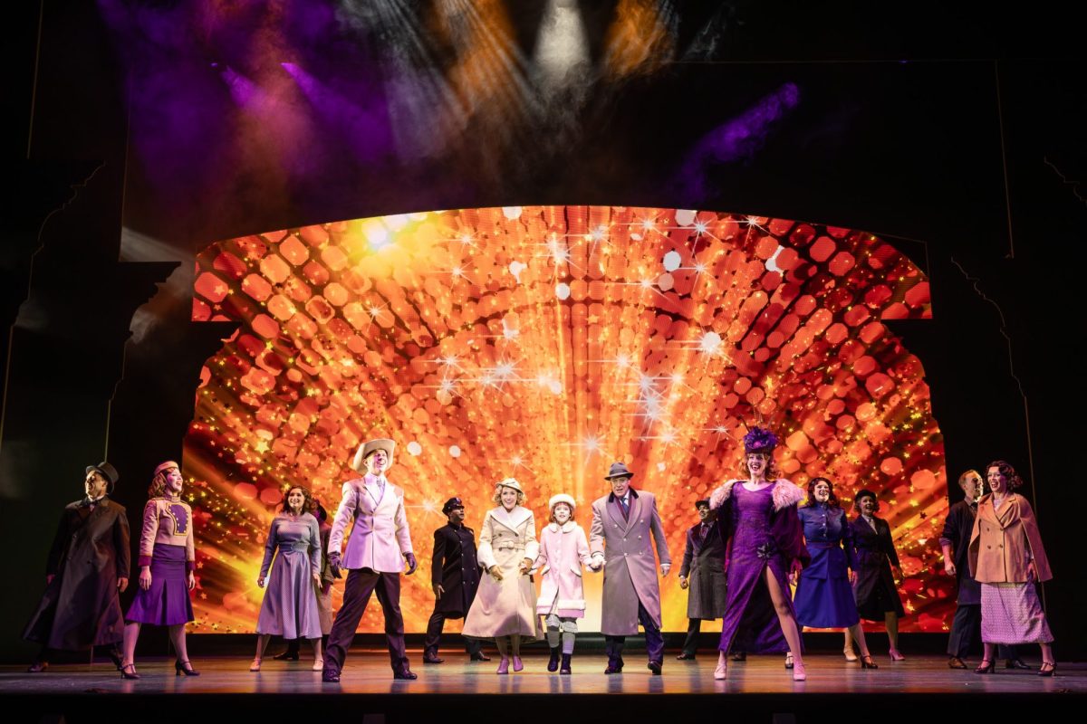 The cast of "Annie" standing against a bright, blazing backdrop.