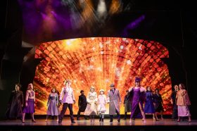 The cast of "Annie" standing against a bright, blazing backdrop.