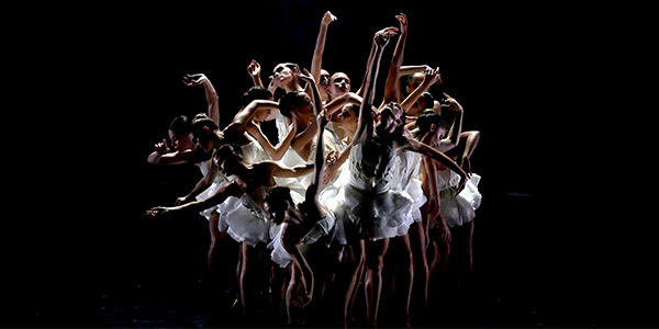 A group of ballerinas mid dance, dressed in white.