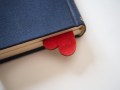 An upside down red heart is peeking from the pages of a blue book.