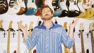 A man in a blue stripey shirt surrounded by guitars.
