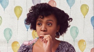 A black woman with frizzy hair blowing on a party popper.