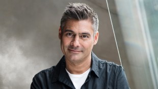 A man wearing a white t-shirt under a charcoal shirt.