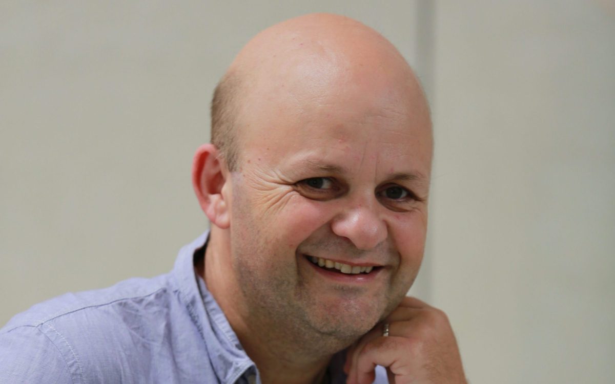 A smiling bald man wearing a light blue shirt.