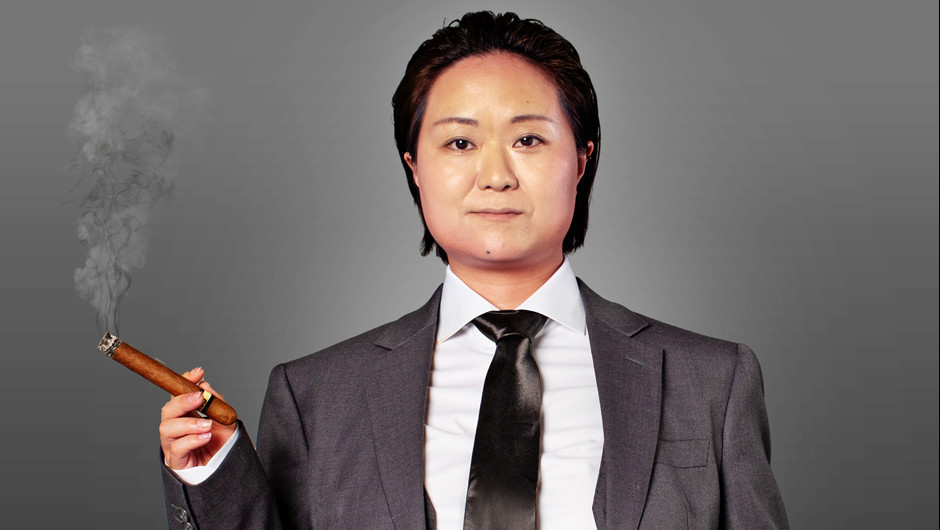 A Chinese woman dressed in a grey suit and black tie and holding a cigar.