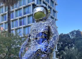 public art: a close up of part of a huge chrome blue and silver metal sculpture of an astronaut figure installed in a park setting.