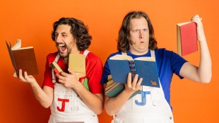 Against an orange backdrop, two men are holding up books. One is wearing a red t-shirt, the other one a blue one. The letter 'J' is printed on the white overalls.