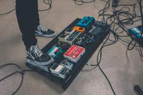 Australian music industry: an audio mixing deck/ PA system on the floor of a stage surrounded by cables with a person's foot on one of the PA system's pedals.