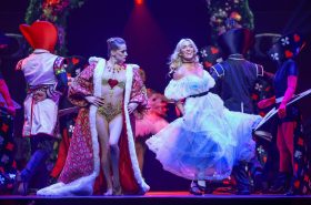 A woman dressed as the Red Queen ( a red robe with white trim over spangled gold costume) and another dressed as Alice (white flouncy dress)