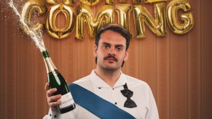 A brunette man with a moustache in white short and a tie askew is holding onto a spraying champagne bottle.