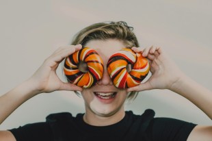 Woman in black t-shirt holding two colourful bagels over her eyes. Arts news watch