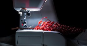 A red flower lies across the spotlight of a sewing machine's needle and thread.