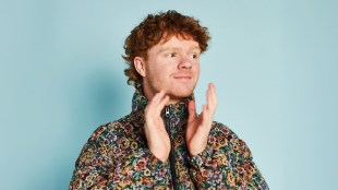 A ginger-headed man mid clap wearing a floral bomber jacket.