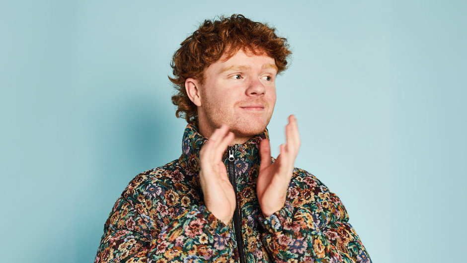 A ginger-headed man mid clap wearing a floral bomber jacket.